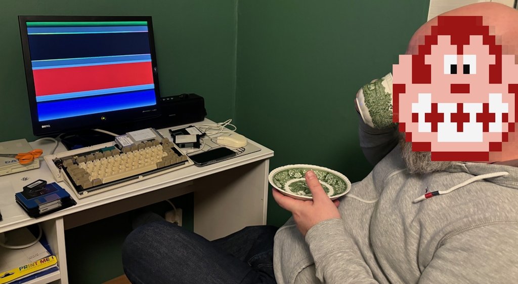 A man is sipping coffee in front of a partially disassembled, but still running, Amiga 600.
